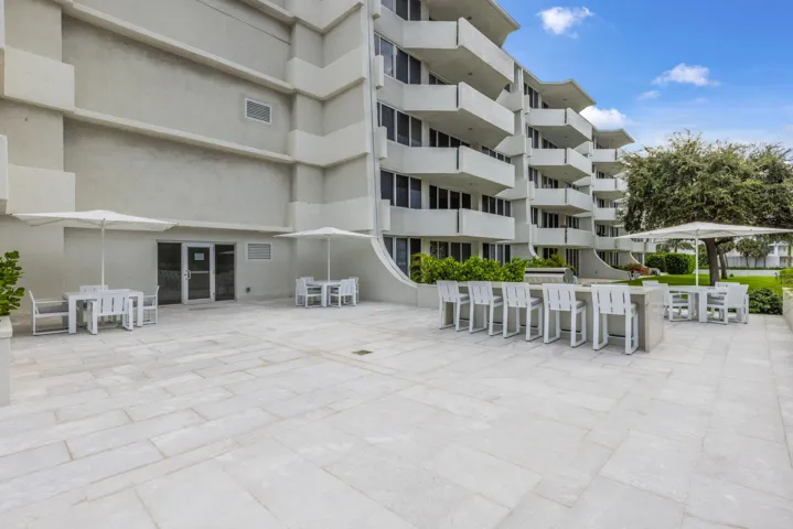 Expansive outdoor patio with stone-finish pavers, multiple seating areas, a built-in bar, and a multi-story building exterior with individual balconies