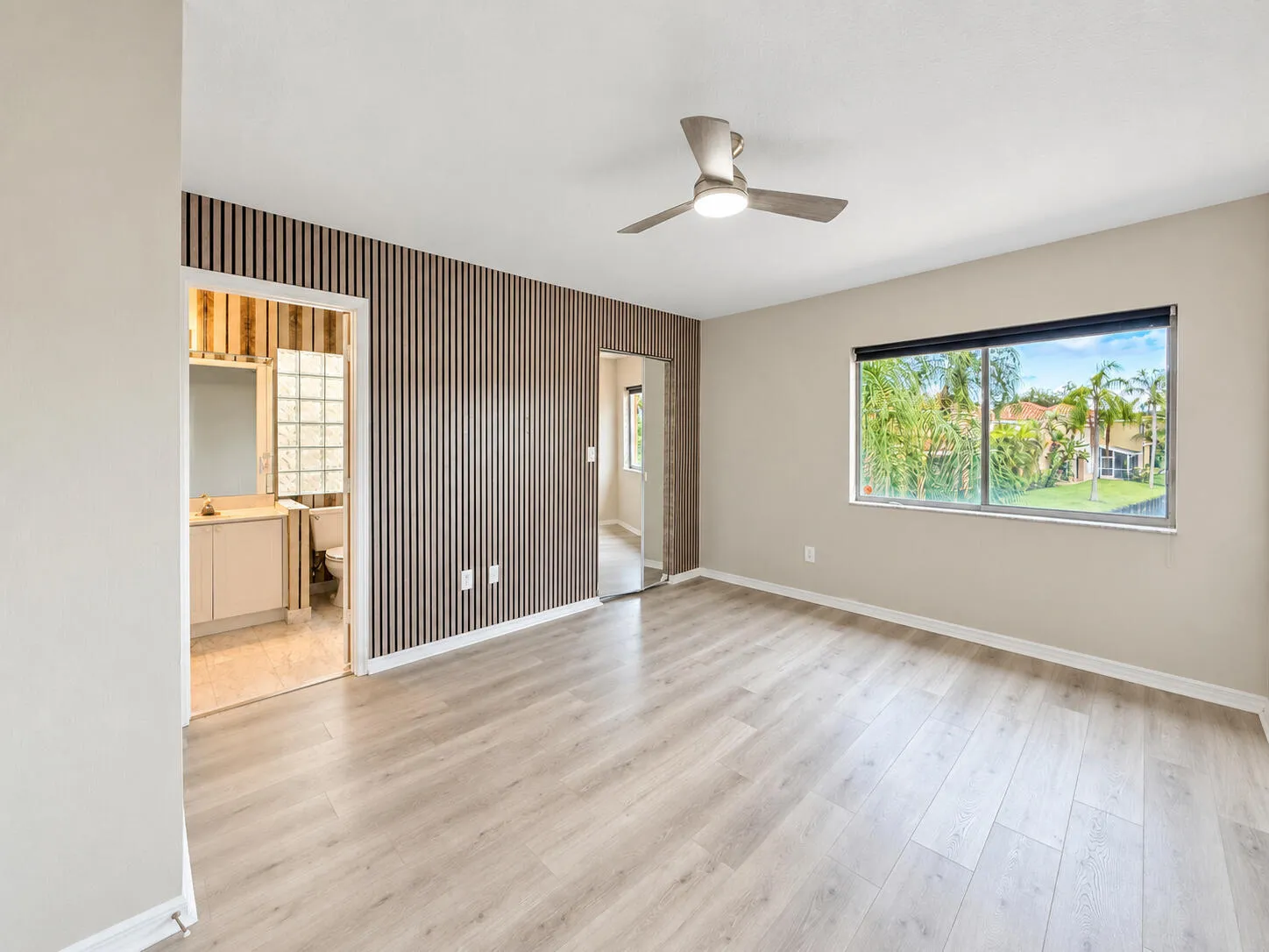 Wood-finish flooring, accent wall with vertical paneling, contemporary ceiling fan, and large window