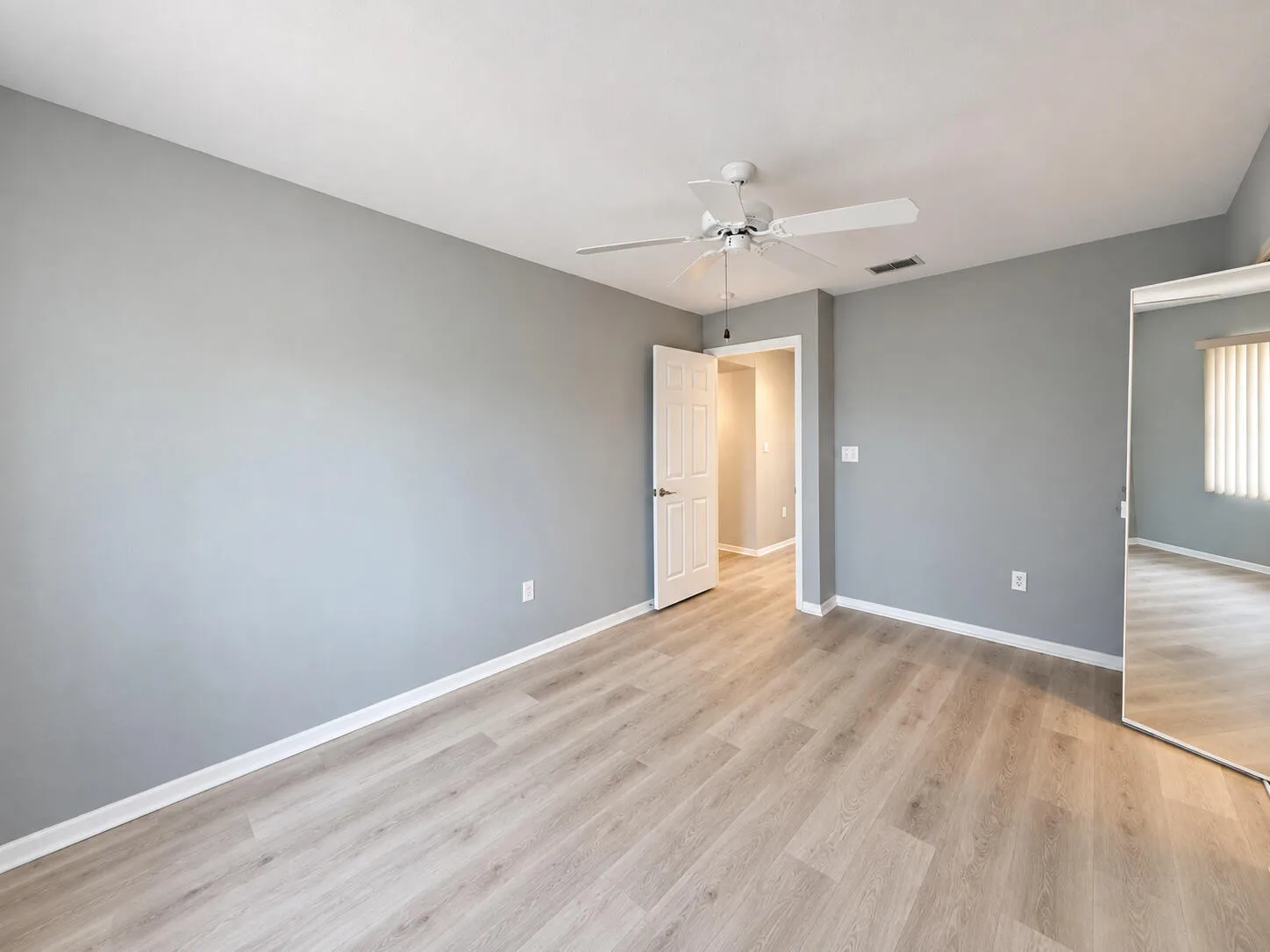 Wood-finish flooring, light grey wall paint, and a ceiling fan with integrated lighting