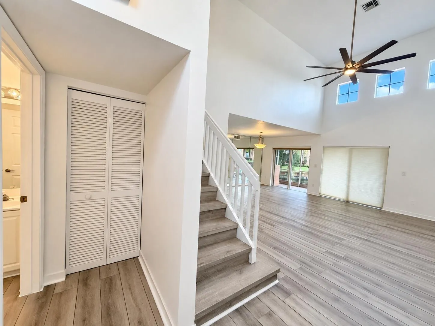 Vaulted ceiling with a ceiling fan, wood-finish flooring, staircase with white railings, louvered bi-fold closet doors, and sliding glass doors