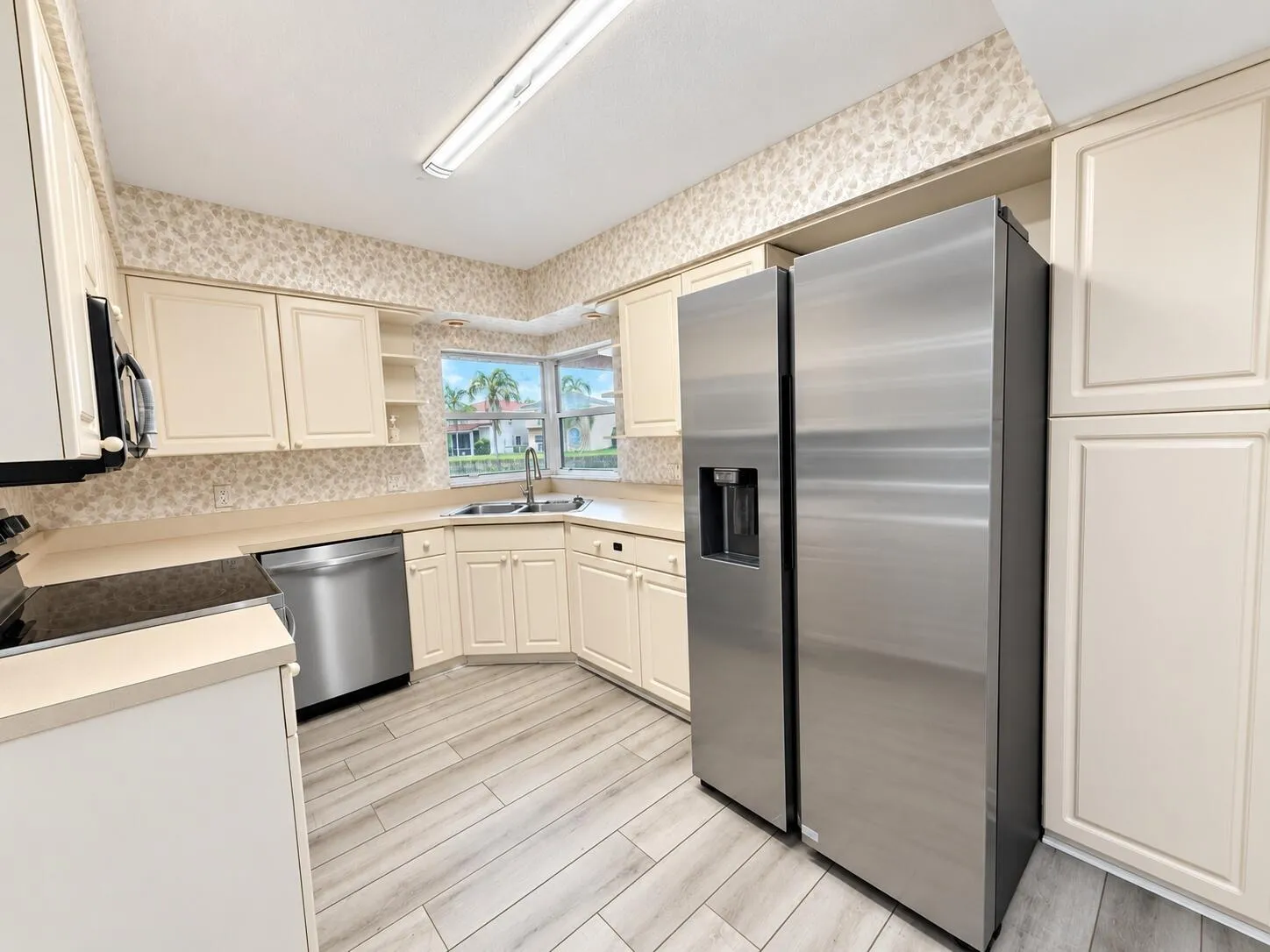 Kitchen with cream cabinetry, stainless steel appliances, light wood-finish flooring, and a double basin sink