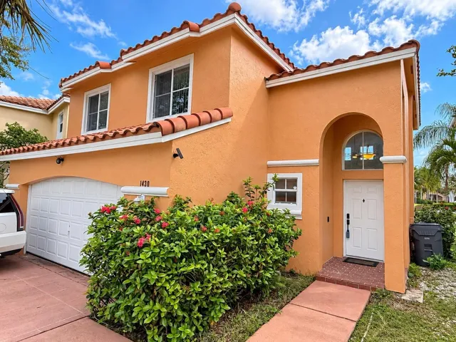 Two-story stucco exterior with a tile roof, an arched entry, a white garage door, and mature landscaping