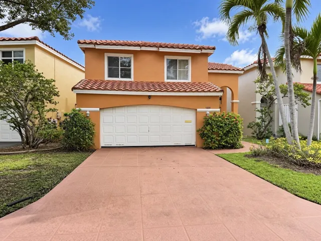Two-story stucco exterior with a terra cotta tile roof, an integrated garage, a paved driveway, and mature landscaping