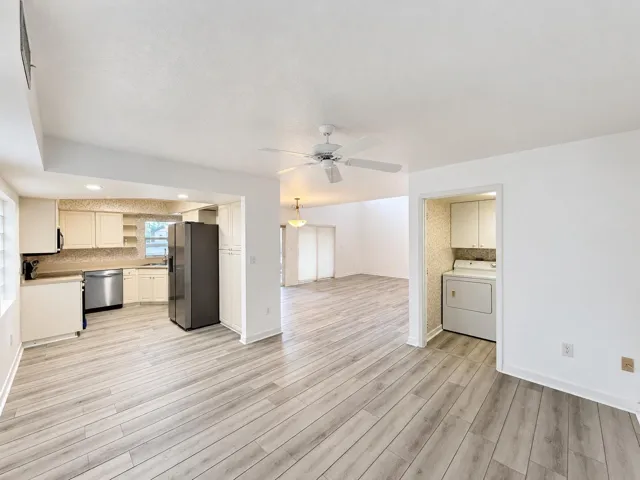 Light wood-finish flooring, recessed lighting, ceiling fan, kitchen with cream cabinetry, and a dedicated laundry area
