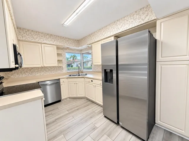 Kitchen with cream cabinetry, stainless steel appliances, light wood-finish flooring, and a double basin sink