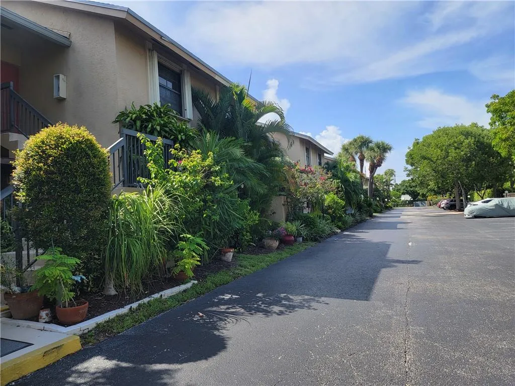 Stucco exterior building with a pitched roofline, surrounded by dense tropical landscaping, paved driveway, and mature trees