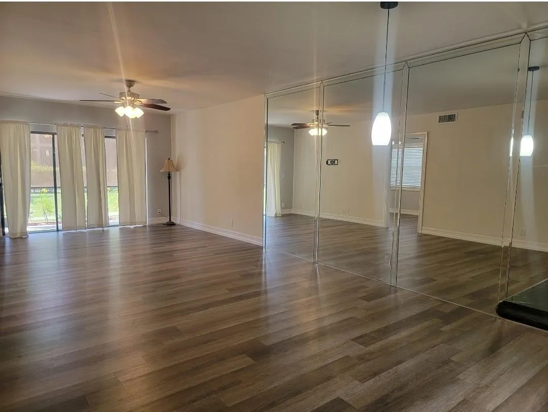 Wood-finish flooring, ceiling fan, mirrored accent wall, and sliding glass doors