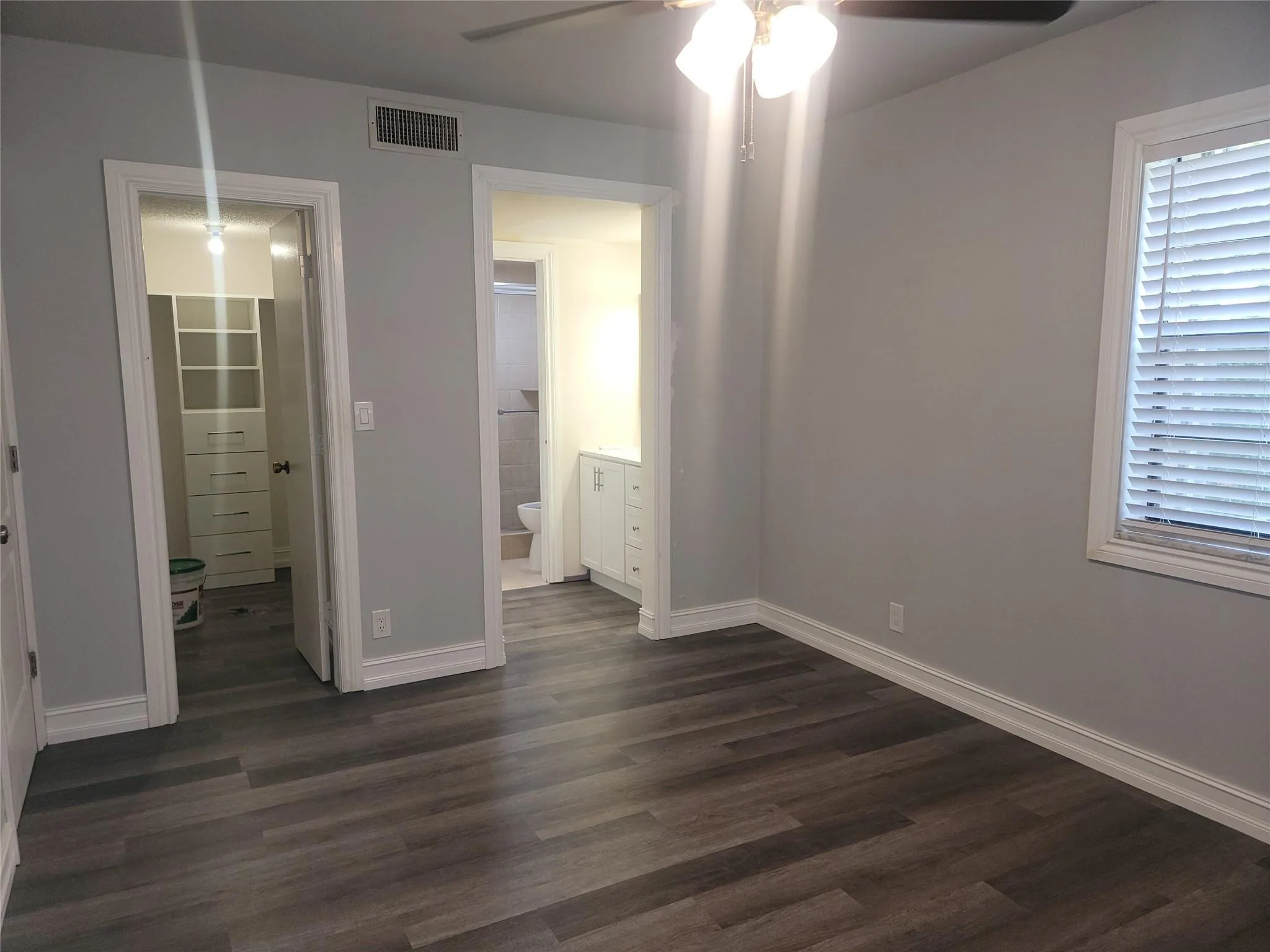 Wood-finish flooring, ceiling fan with integrated lighting, window with blinds, base molding, and built-in closet organization system