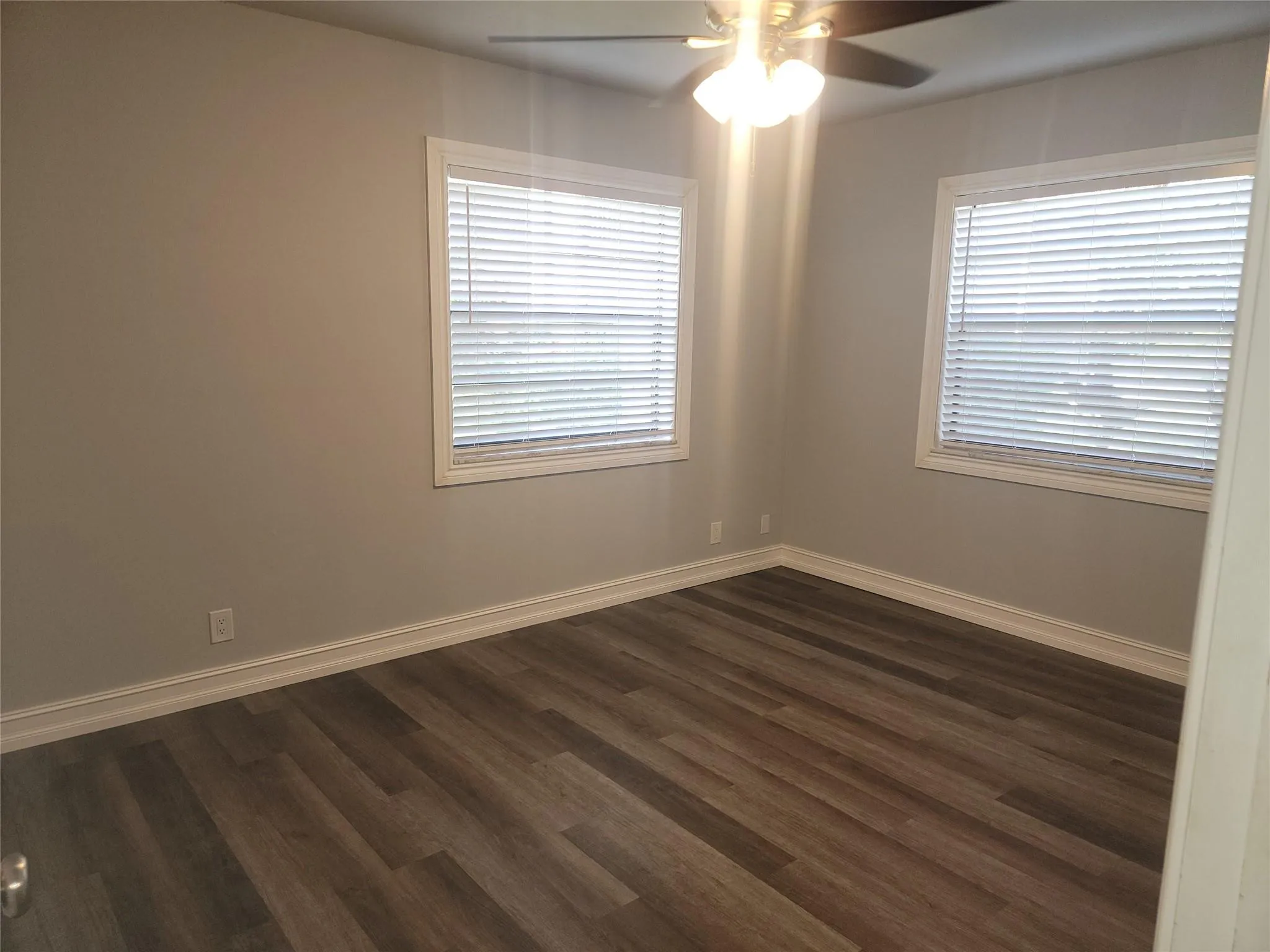 Wood-finish flooring, neutral wall tones, two windows with blinds, and a ceiling fan with integrated lighting