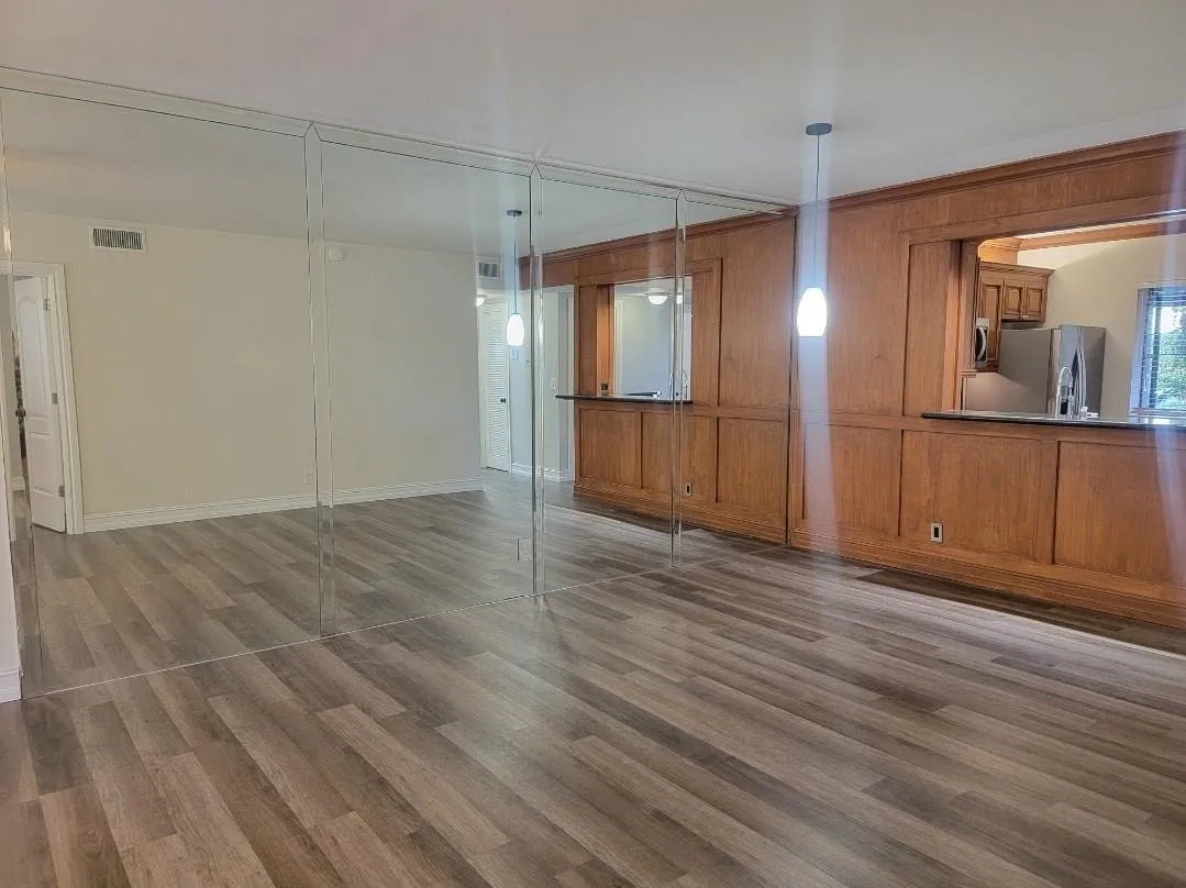 Wood-finish flooring, full-height mirror wall, wood paneling, built-in cabinetry, and pendant lighting