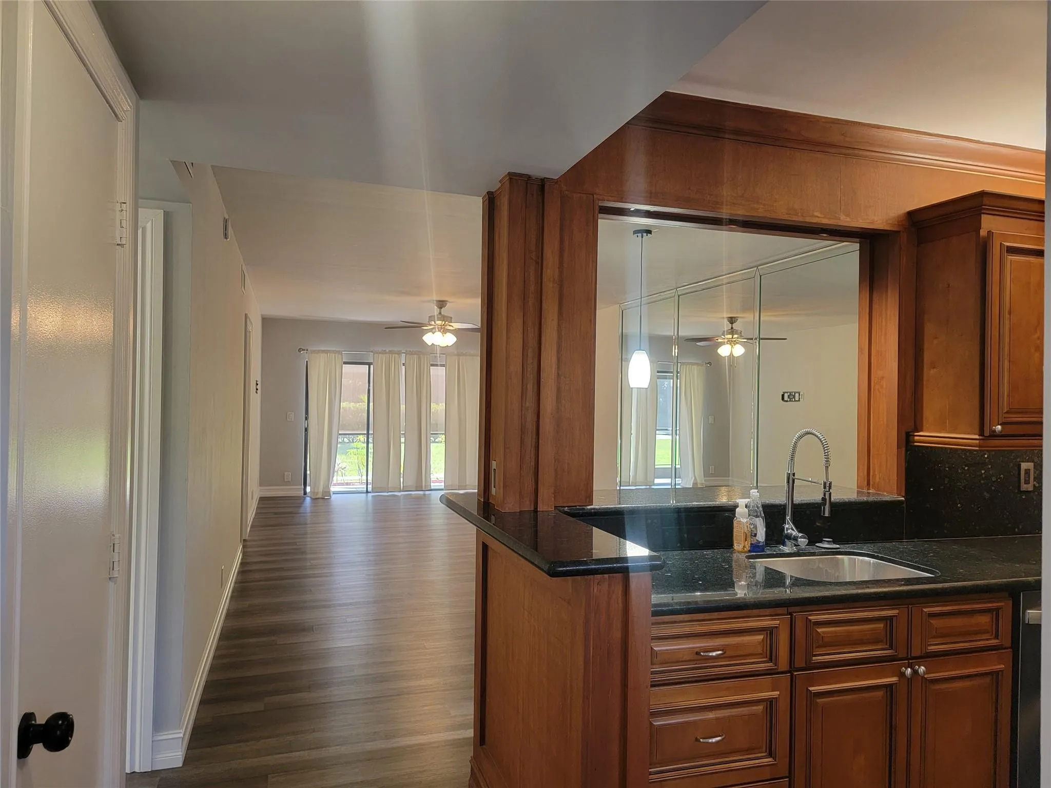 Kitchen pass-through with wood cabinetry, dark countertops, and a stainless steel sink