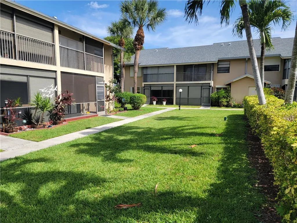 Manicured lawn with mature palm trees, paved walkways, and screened lanais
