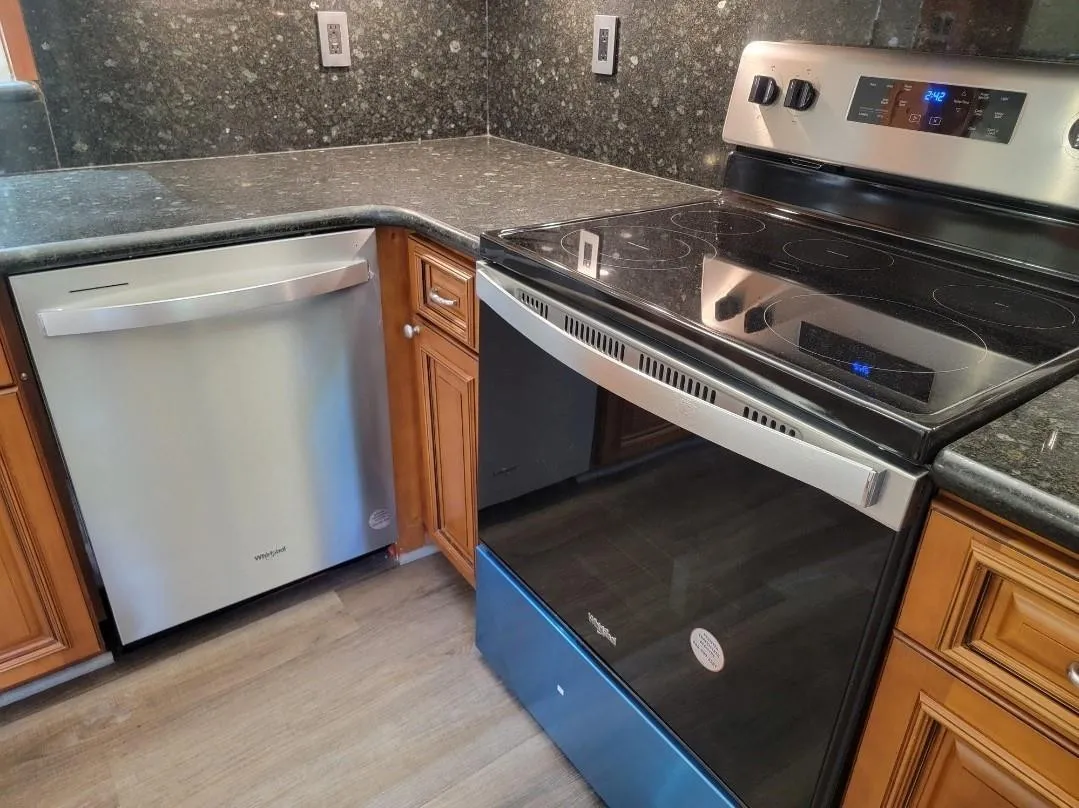 Stainless steel dishwasher, coordinating stainless steel range with ceramic cooktop, stone-finish countertops, wood cabinetry, and wood-finish flooring