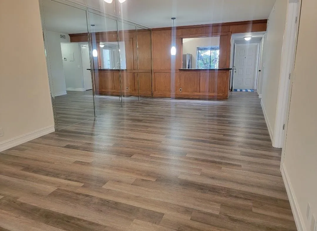 Wood-finish flooring throughout, mirrored accent wall, and built-in wood cabinetry with a serving bar