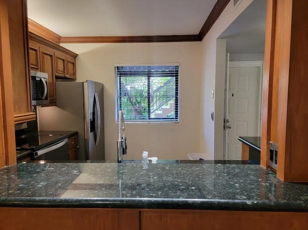 Kitchen featuring wood cabinetry, dark speckled countertops, stainless steel appliances, and a window with horizontal blinds