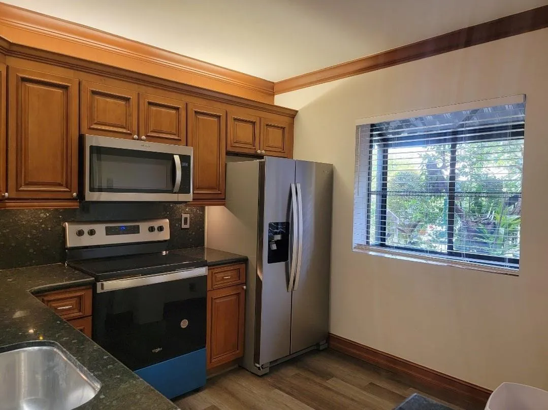 Wood-finish cabinetry with crown molding, stainless steel appliances, dark stone countertops, stainless steel sink, and wood-finish flooring