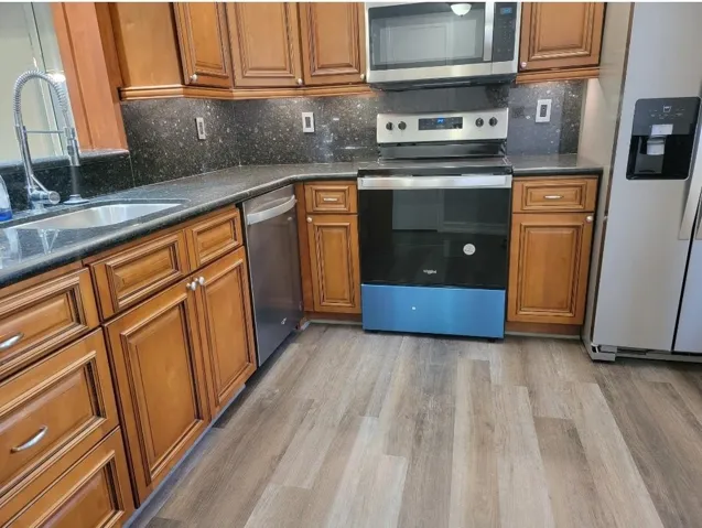 Full kitchen featuring wood-finish cabinetry, dark countertops, a stainless steel sink, and stainless steel appliances
