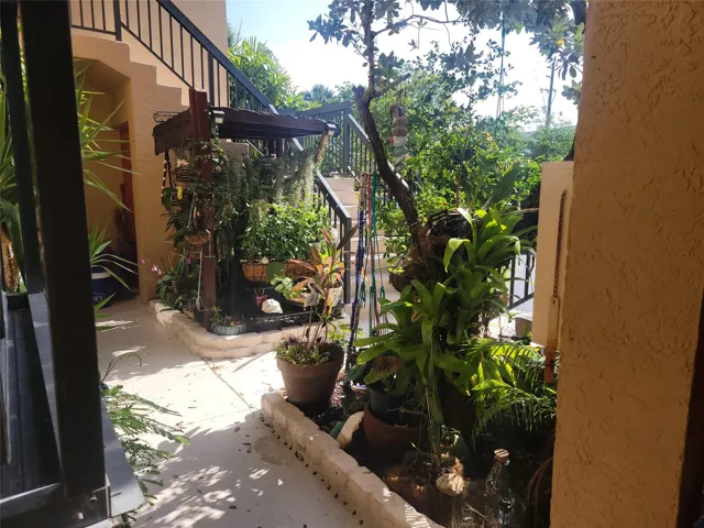 Staircase with wrought iron railing, stucco exterior, and planted garden beds