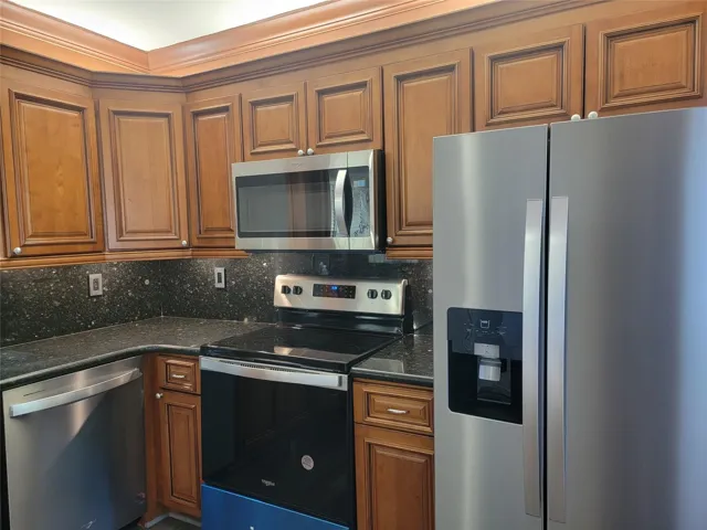 Kitchen featuring stainless steel appliances, dark stone countertops, wood cabinetry, and a built-in microwave
