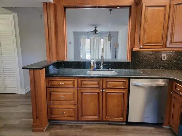 Kitchen featuring wood-finish cabinetry, dark speckled countertops, a stainless steel sink, and a stainless steel dishwasher