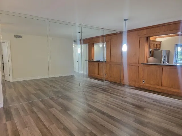 Wood-finish flooring, full-height mirror wall, wood paneling, built-in cabinetry, and pendant lighting