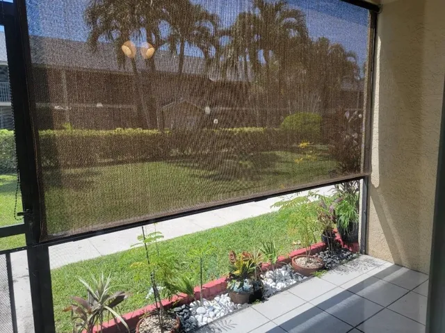 Screened patio featuring a roller shade, tiled flooring, and a landscaped planter bed with white stones