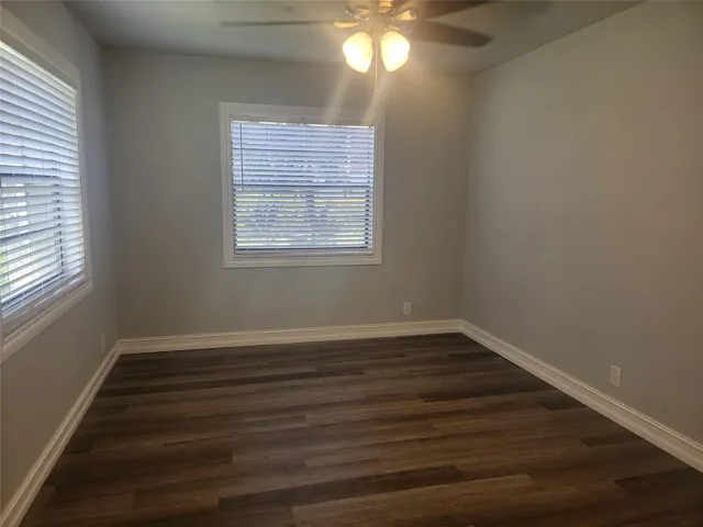 Wood-finish flooring, two windows with blinds, ceiling fan with integrated lighting, and neutral wall tones