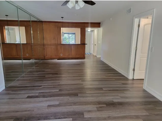 Wood-finish flooring throughout, mirrored wall panels, wood paneled wall with pass-through openings, white trim, and a ceiling fan