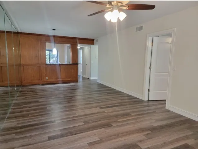 Wood-finish flooring, wood paneling, mirrored wall, ceiling fan with integrated lighting, and white interior doors