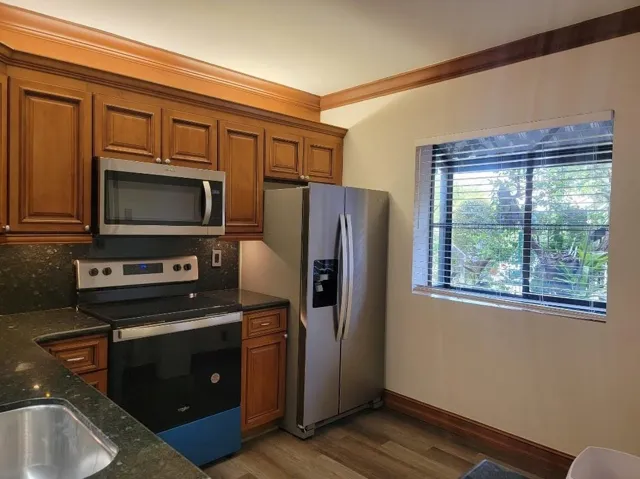 Wood-finish cabinetry with crown molding, stainless steel appliances, dark stone countertops, stainless steel sink, and wood-finish flooring