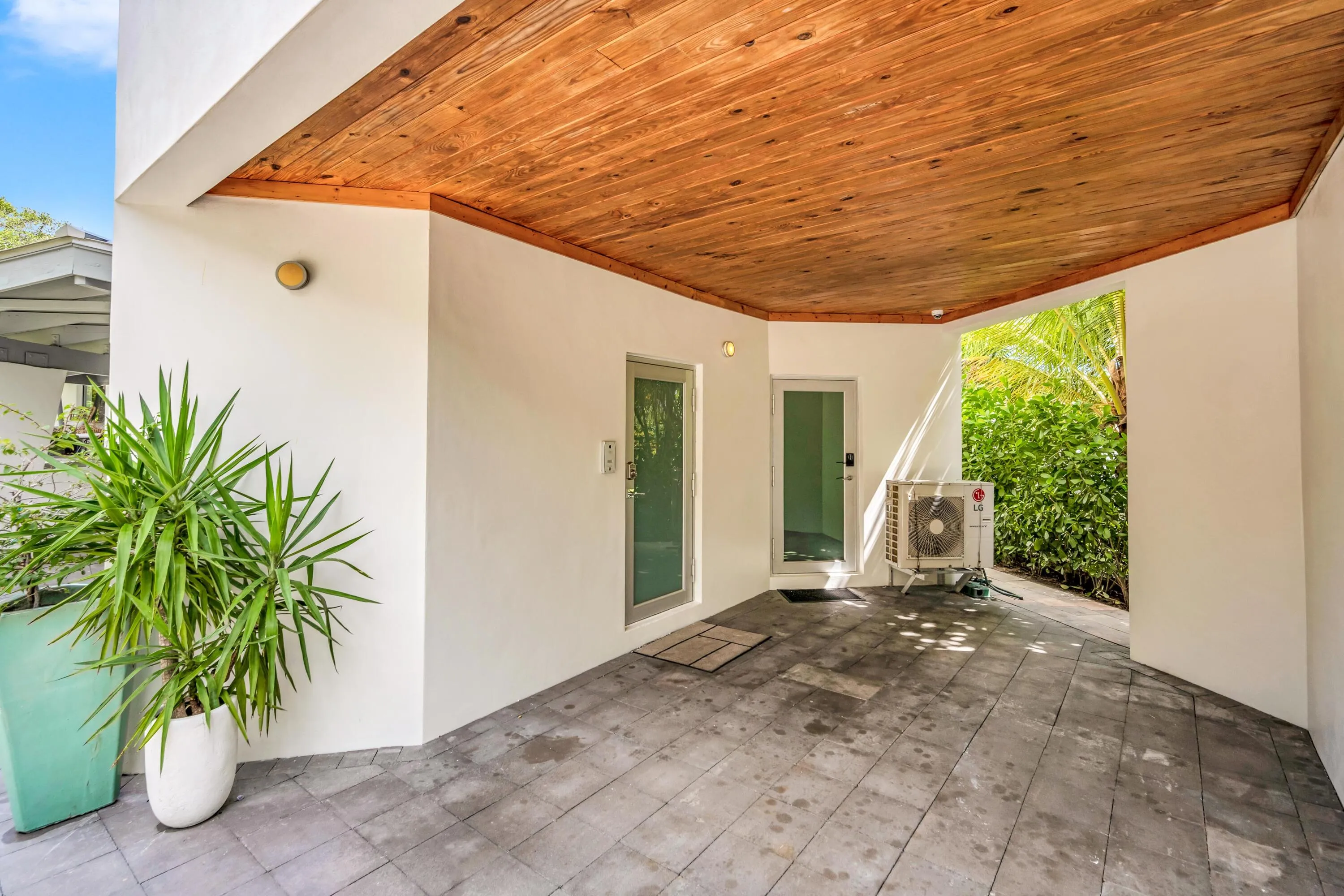 Covered patio featuring a wood-finish ceiling, light gray paver flooring, white stucco walls, and two exterior doors with frosted glass​​‌​​​​‌​​‌‌​‌‌​​​‌‌​‌​‌​‌​​​‌​​ panels