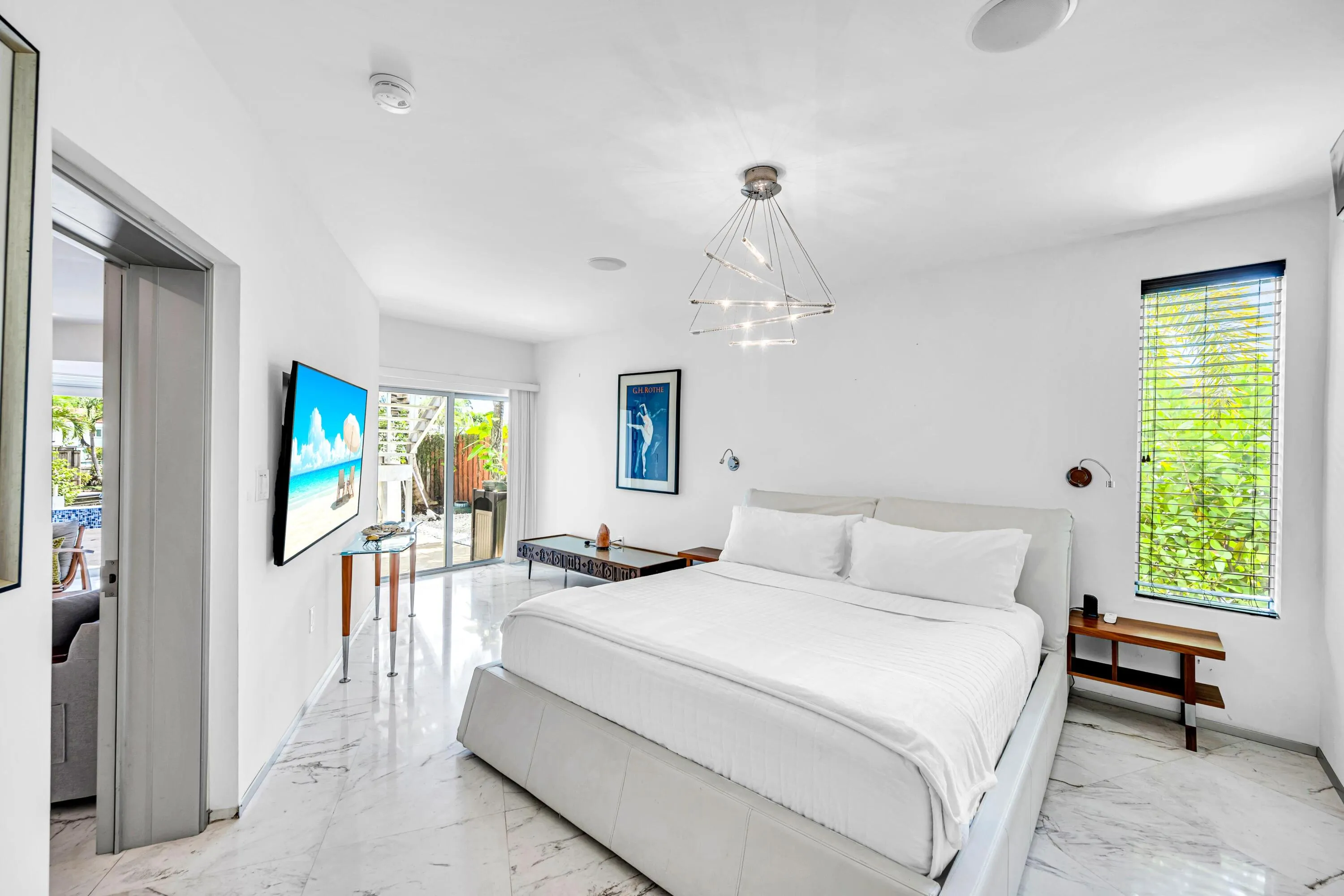 Bright interior with white walls, sliding glass doors, white marble-look tile flooring, and a modern geometric light fixture
