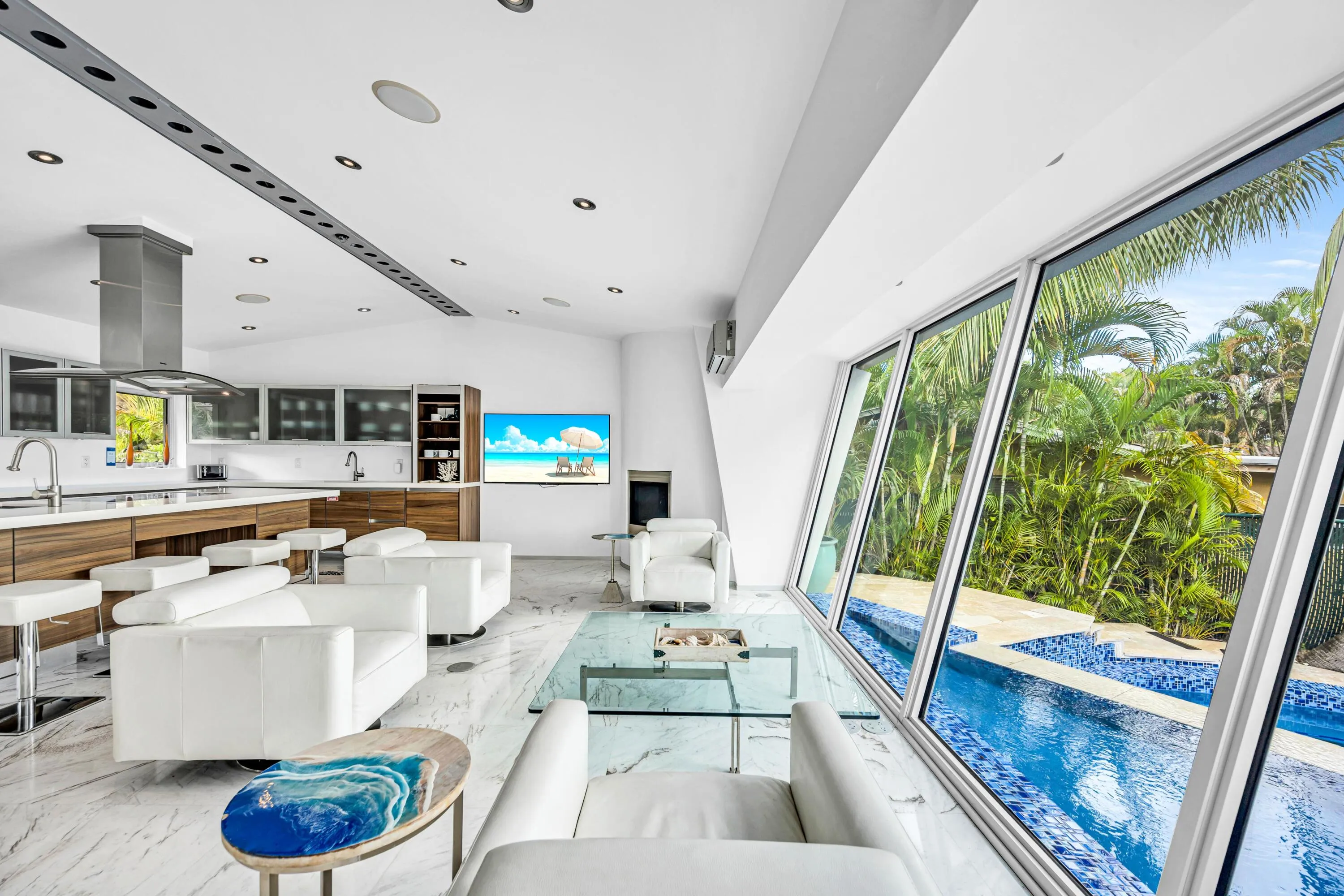 Open-concept living space with large format tile flooring, a contemporary kitchen featuring a stainless steel range hood, and extensive floor-to-ceiling windows overlooking a built-in swimming pool