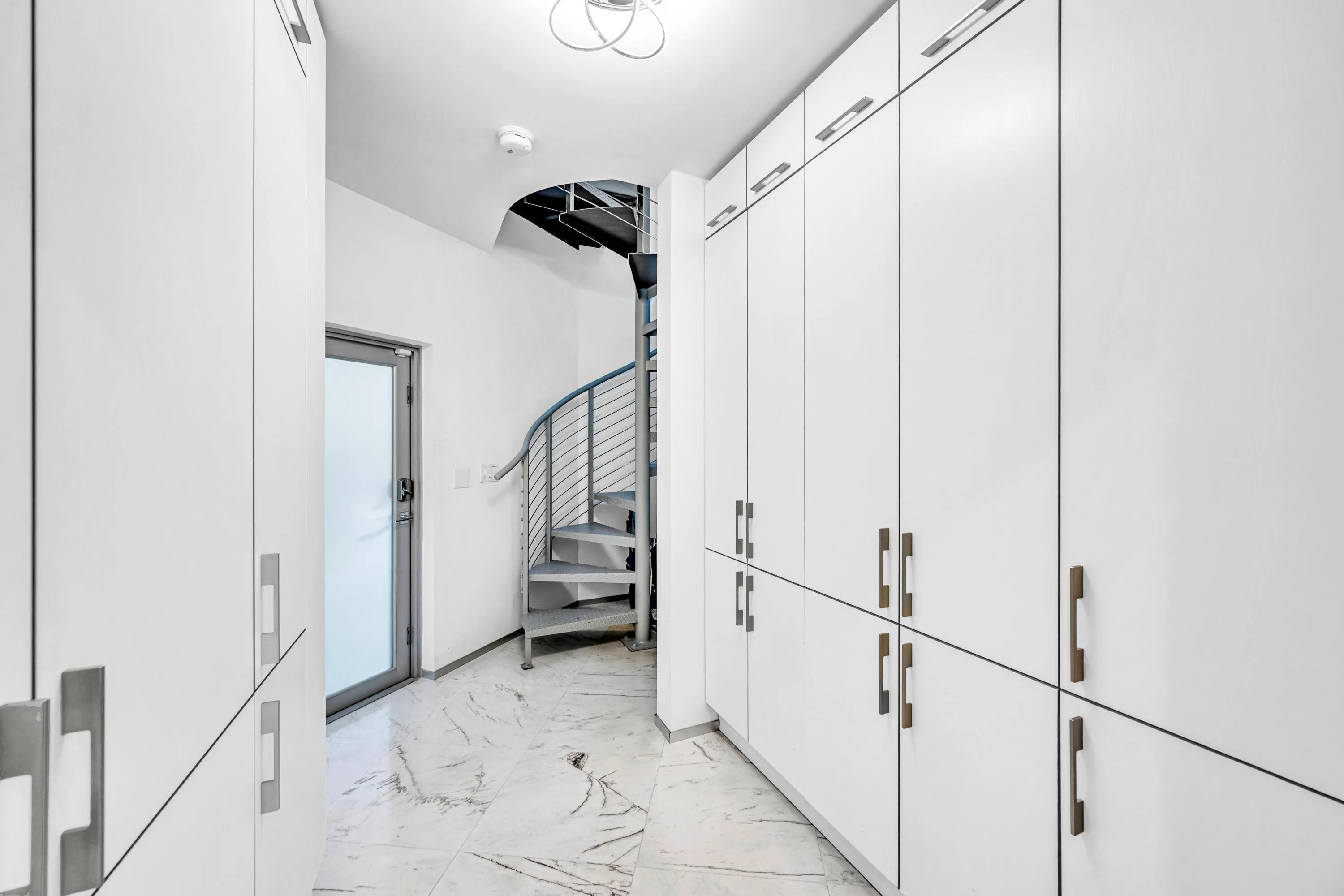 Custom built-in storage cabinetry, polished tile flooring, contemporary spiral staircase, and modern door with frosted glass