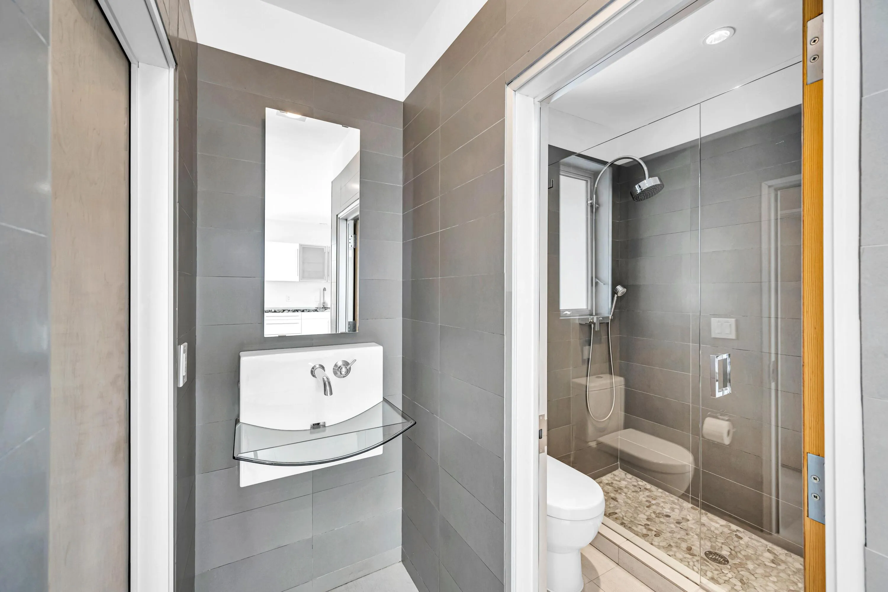 Modern bathroom featuring gray tiled walls, a wall-mounted sink with a glass shelf, and a mirror