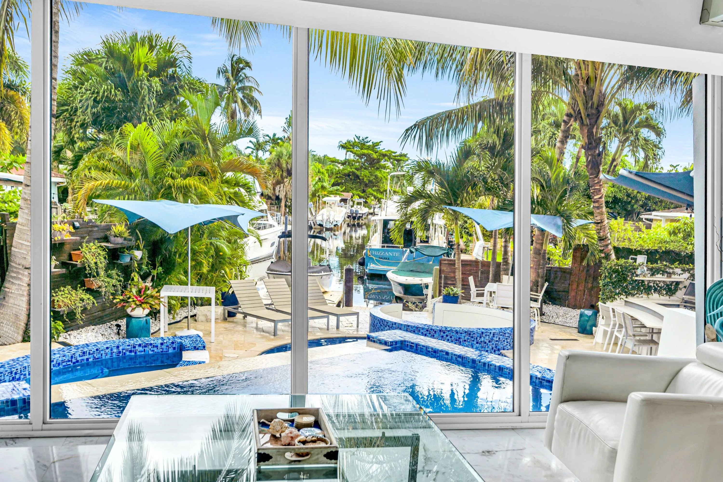 Floor-to-ceiling windows with expansive water frontage, a built-in pool, and a spa featuring blue mosaic tile