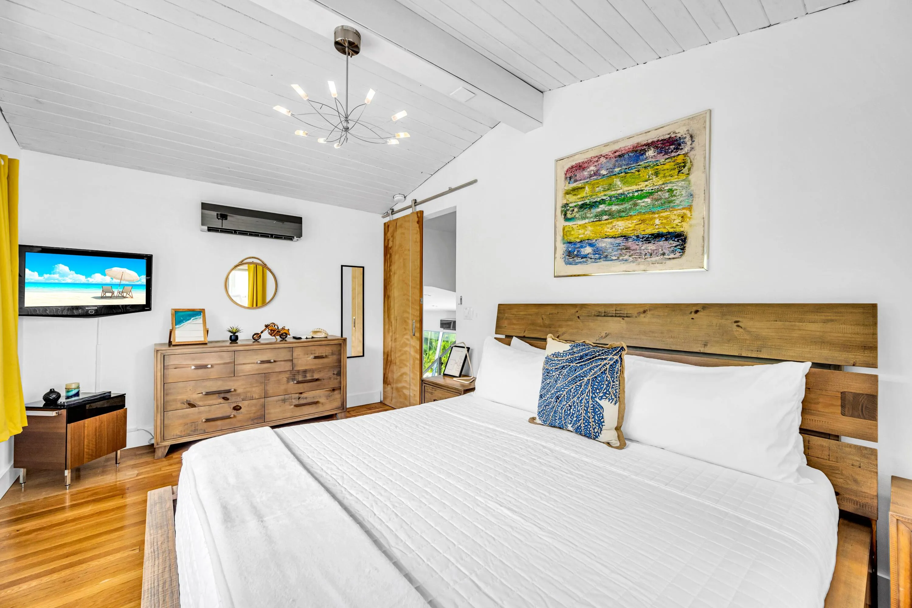 Vaulted wood-paneled ceiling, wood-finish flooring, ceiling-mounted light fixture, wall-mounted air conditioning unit, and a barn door