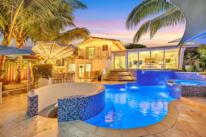 Resort-style backyard featuring a multi-level pool with integrated spa, waterfall features, and blue mosaic tile accents