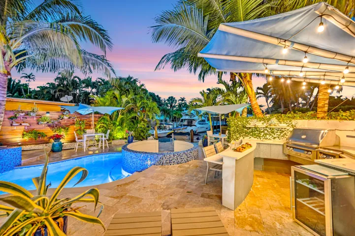Resort-style outdoor living area with a built-in grill station, outdoor bar, and integrated pool