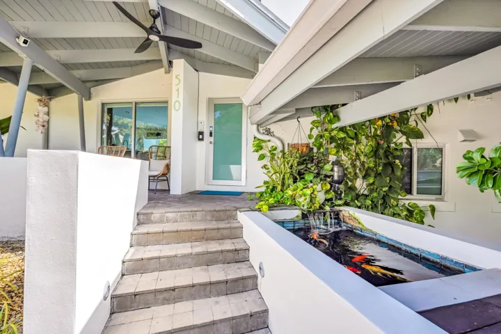Covered entry with exposed beam ceiling, built-in koi pond with waterfall feature, and paver steps