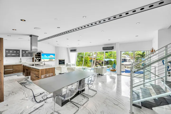 Open-concept living area with polished marble flooring, a modern kitchen island with wood-finish cabinetry, a stainless steel range hood, and a contemporary glass and metal staircase