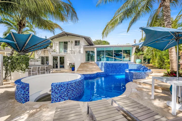 Backyard oasis featuring a curvilinear pool with blue mosaic tiling, integrated spa, and an elevated sundeck