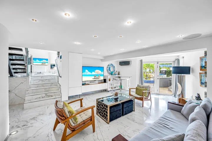 Recessed lighting, marble-style flooring, white walls, built-in media console, and glass doors opening to an exterior area