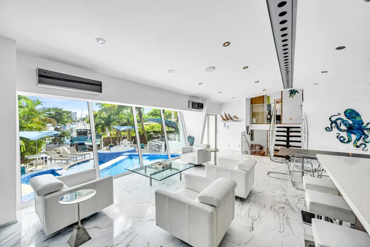 Expansive floor-to-ceiling windows, white marble-finish flooring, recessed lighting, built-in bar, and a geometric staircase