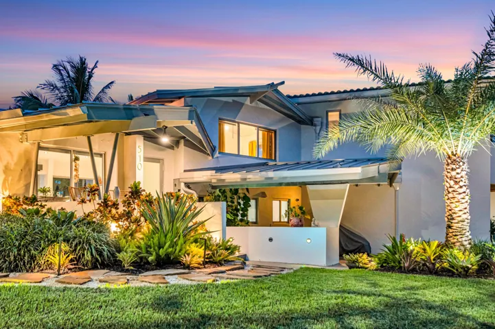 Modern exterior architecture with multiple rooflines, lush landscaping, exterior lighting, an expansive lawn, and a prominent palm tree