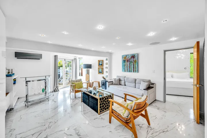 Recessed lighting, large format stone-finish tile flooring, wall-mounted air conditioning unit, glass sliding doors, and a wood door frame