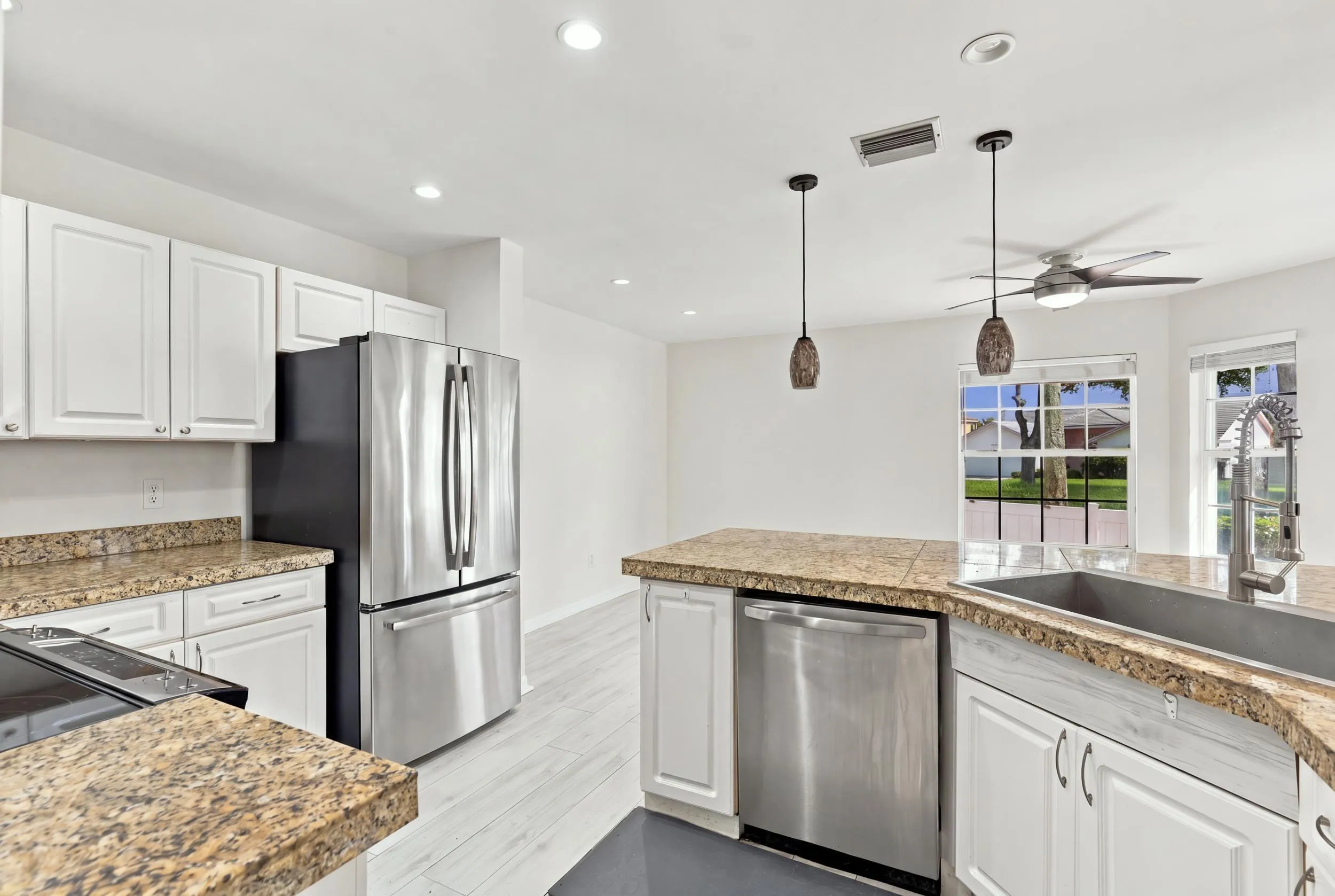 The bright eat-in kitchen features contemporary white cabinetry, granite countertops, new stainless steel appliances, and a convenient breakfast bar. Abundant natural light, space for casual dining, and sliding glass doors create a seamless connection to the private backyard.