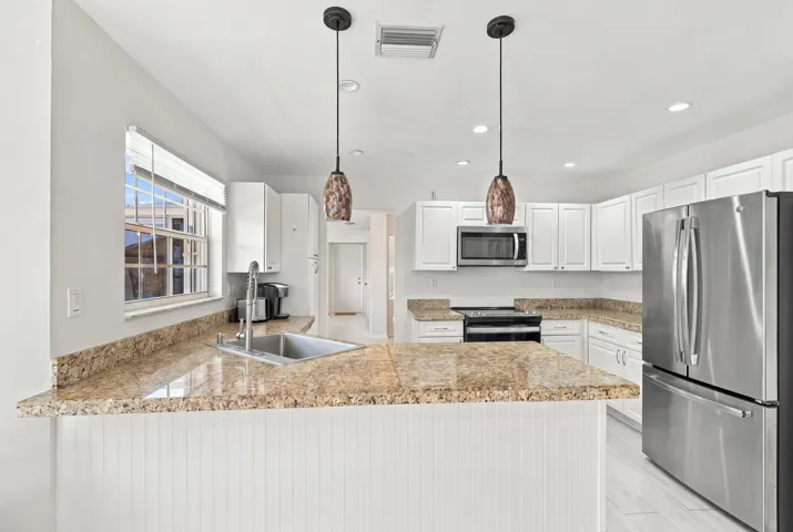 The bright eat-in kitchen features contemporary white cabinetry, granite countertops, new stainless steel appliances, and a convenient breakfast bar. Abundant natural light, space for casual dining, and sliding glass doors create a seamless connection to the private backyard.
