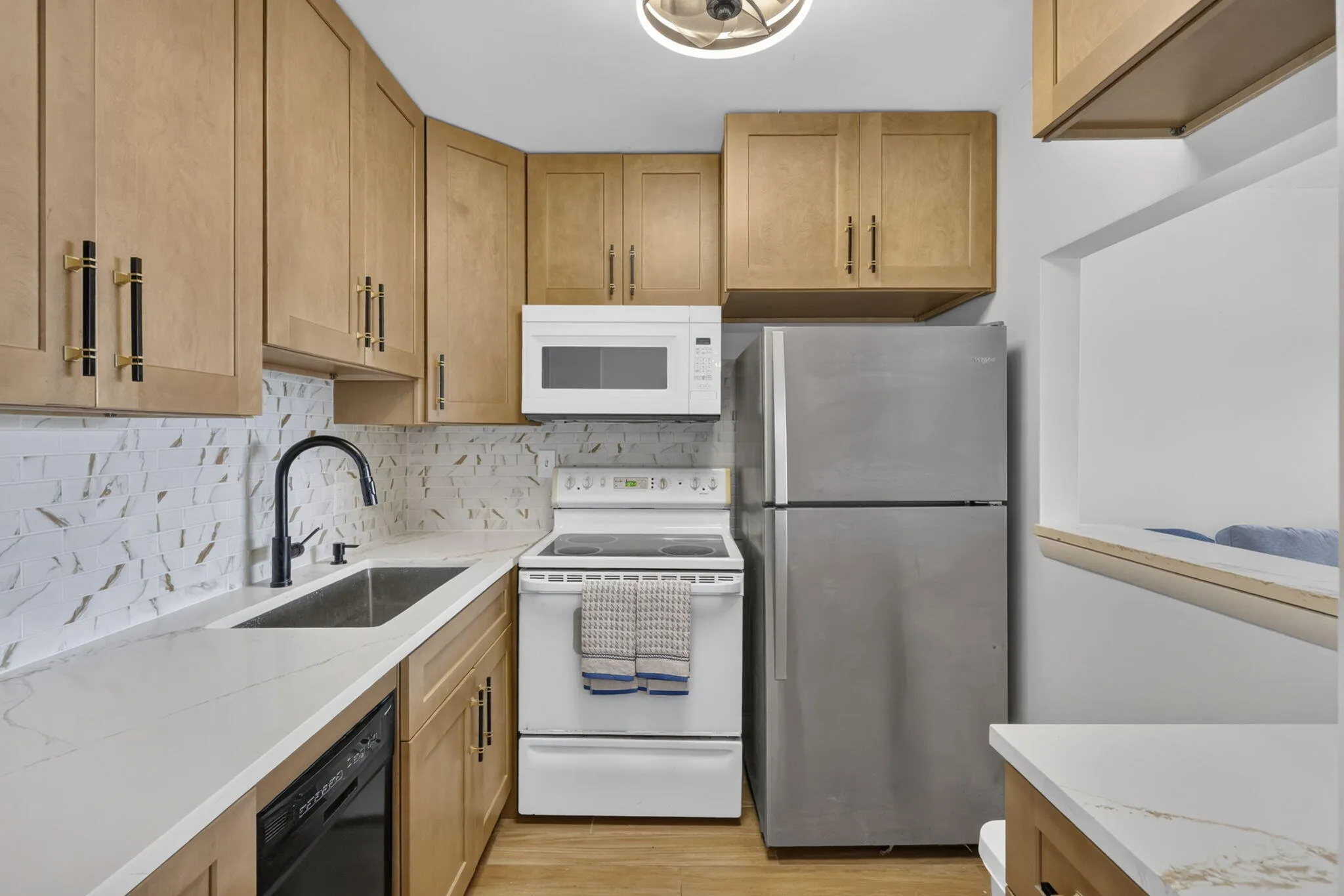 Light wood-finish cabinetry, white quartz countertops, stainless steel refrigerator, white electric range, and a black single-basin sink with a matte black faucet