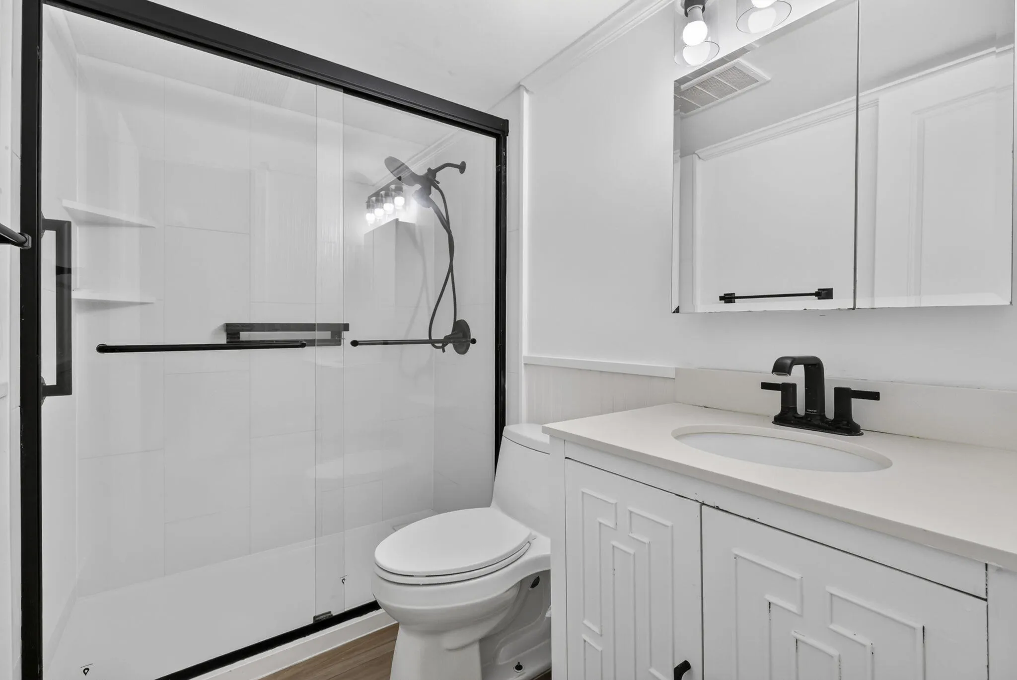 Bathroom featuring a glass-enclosed shower with black trim, a white vanity with paneled doors, a white countertop, and a black faucet
